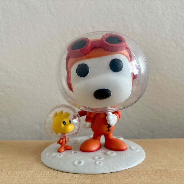 A Funko Pop of Snoopy and Woodstock from Snoopy in Space on a light wood table.