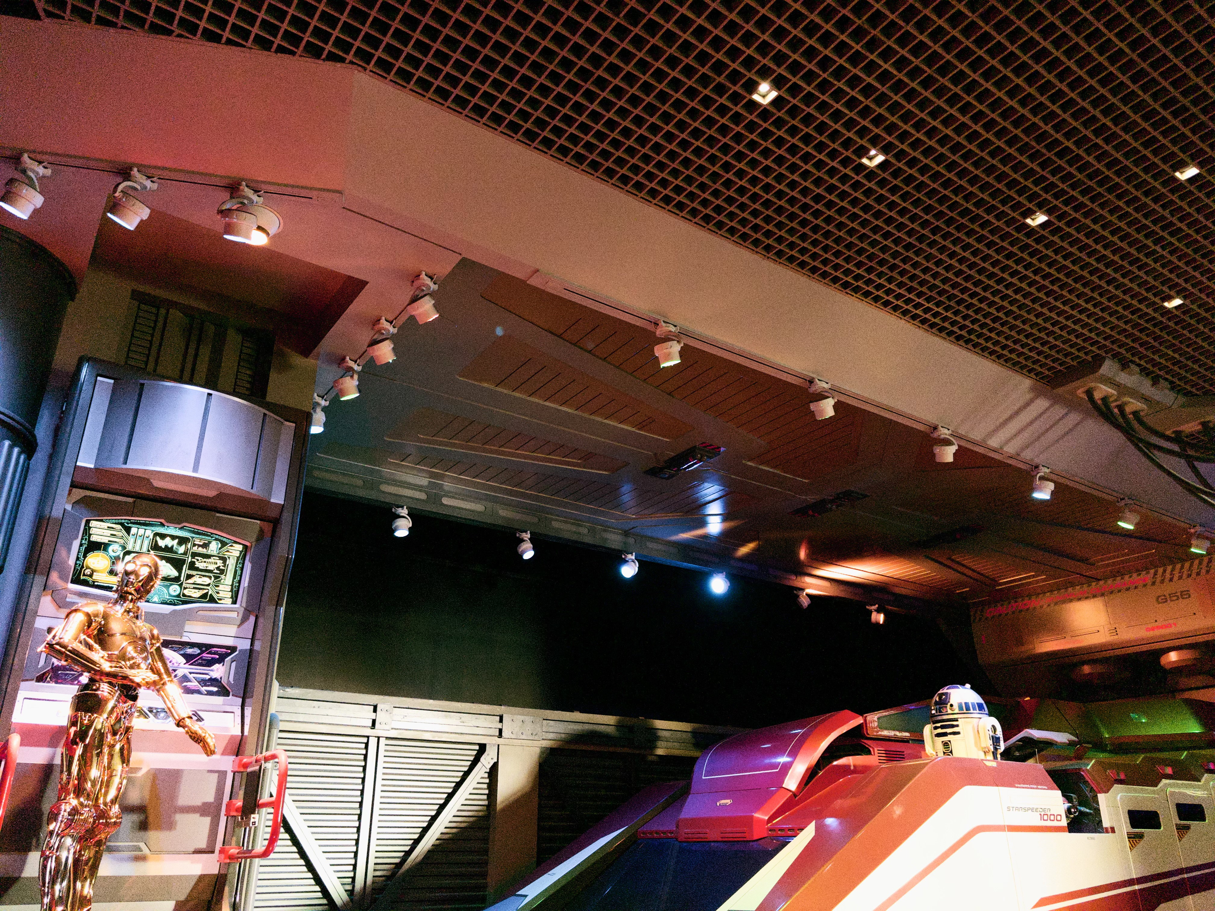 In the Star Tours line, C-3PO stands at a console while R2-D2 is loaded into the Starspeeder 1000.
