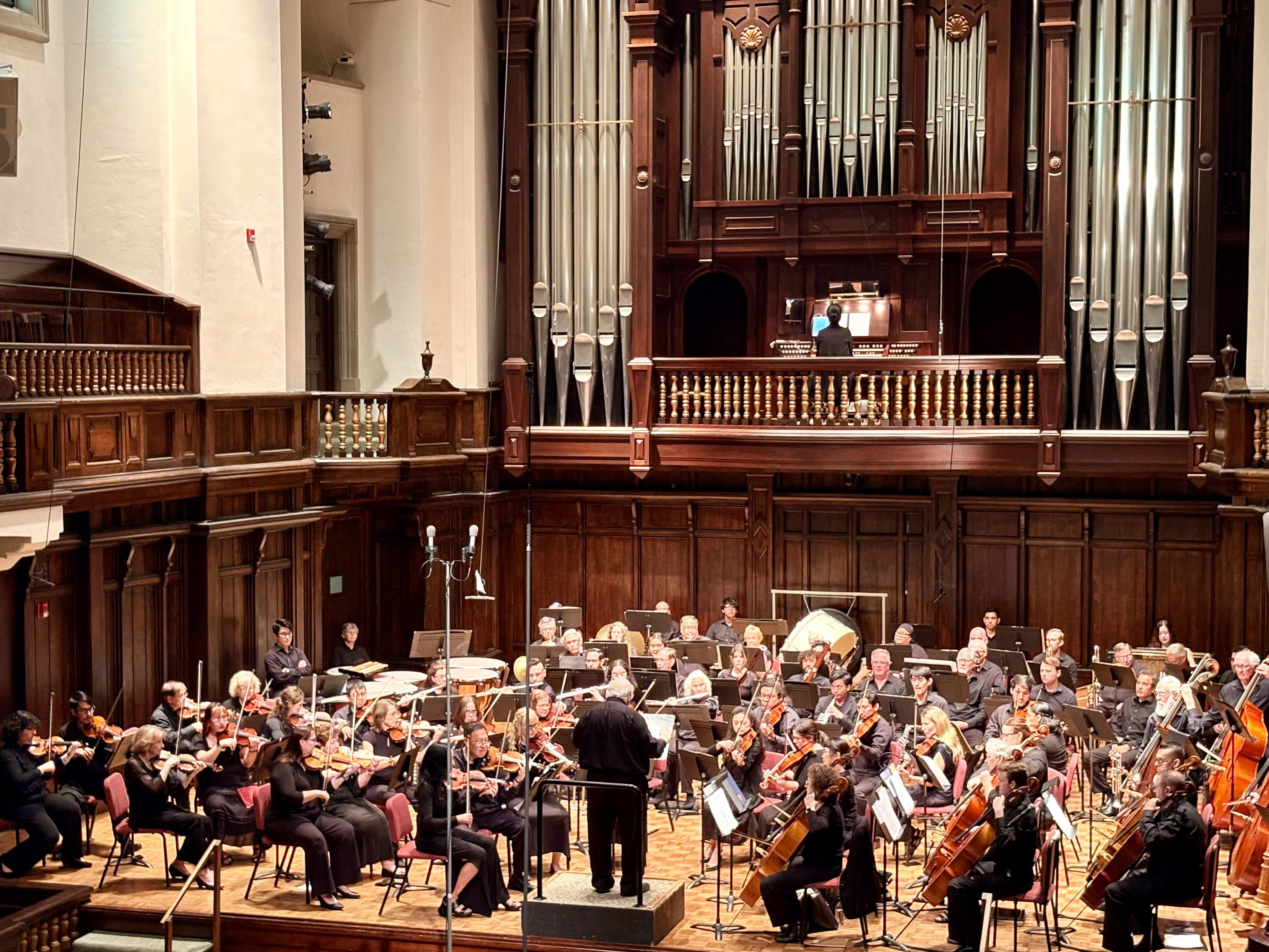 A orchestra performs on a stage below an organ.