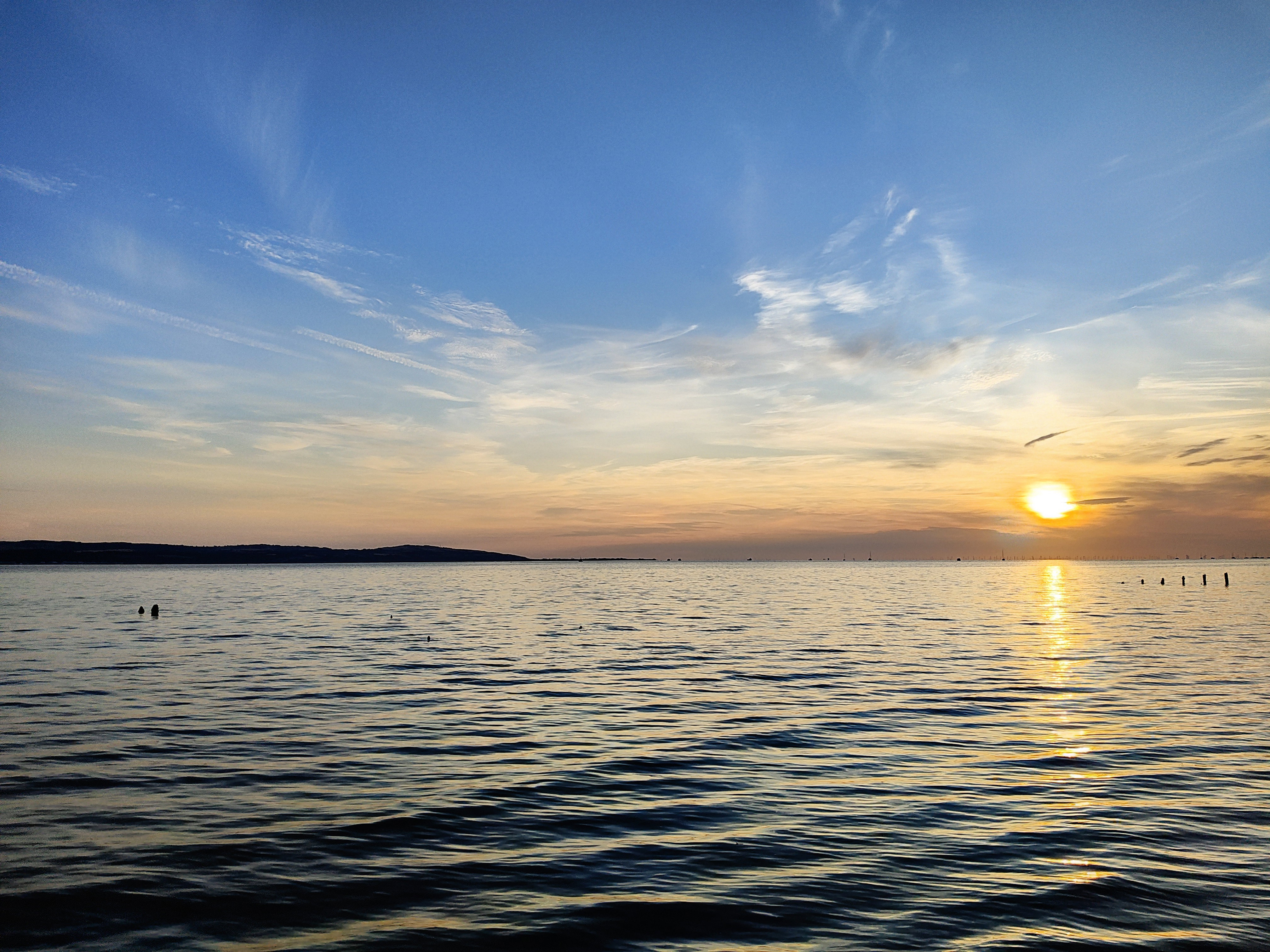 The sun is setting over a rising tide. The sun is at the right of the picture and is reflecting into the water, which covers the lower half of the photo. The sky is a mix of sunset colours.