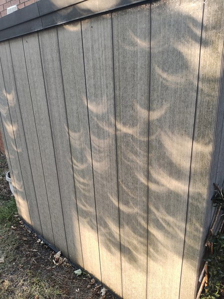 The wall of a shed in the sunlight, where the near total occlusion of the sun by the eclipse of 2026.08.12 can be very clearly seen in multiple places.