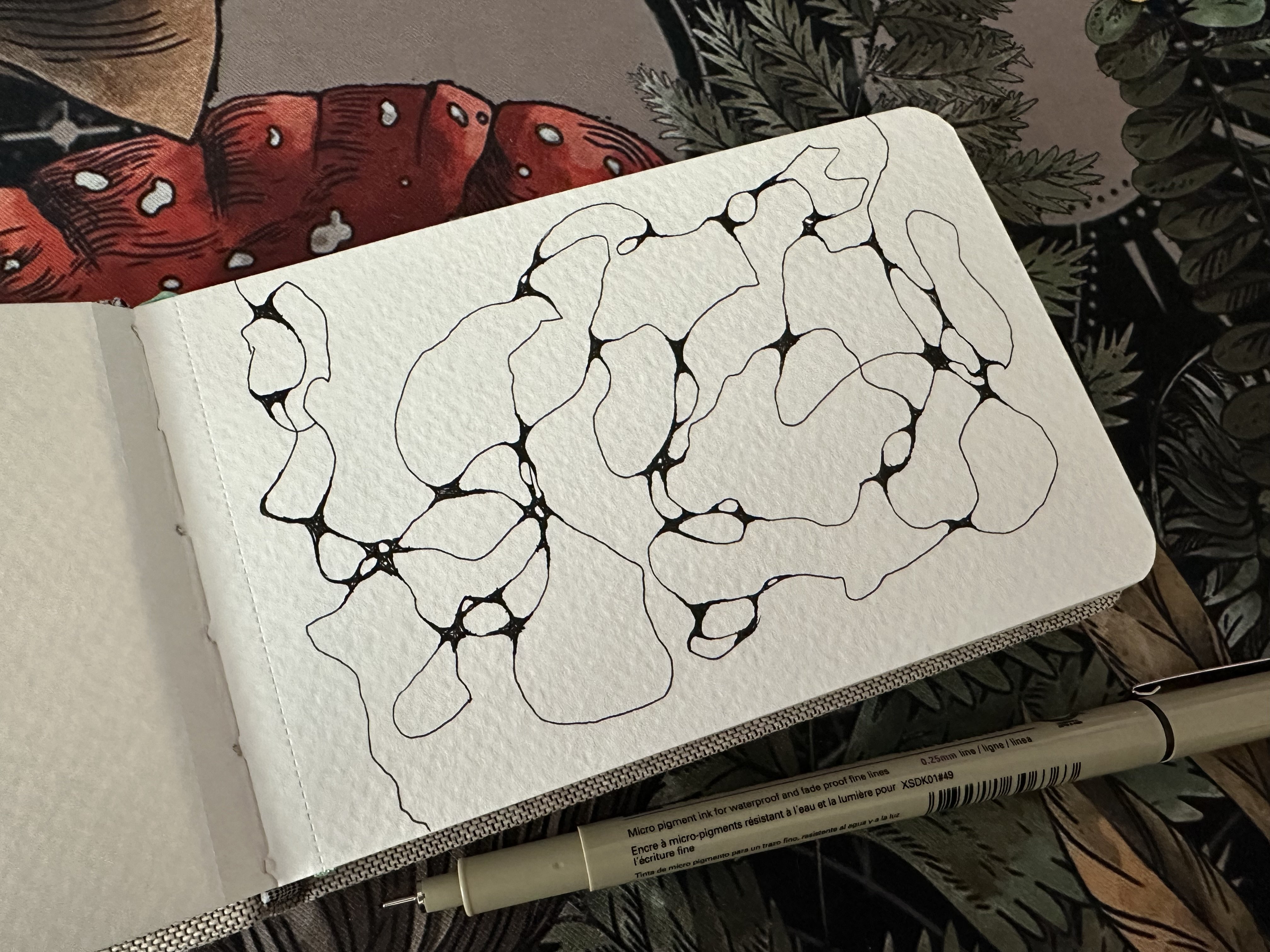 White page in a small notebook with a neurographic drawing in blank ink and a Micron 01 pen beside it.