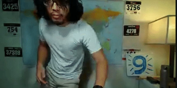 Miguel a masculine Filipino man with black hair and glasses is dancing indoors in front of a map.