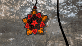 a blinking USB-powered mini Filipino parol hanging by a window looking outside into the daytime