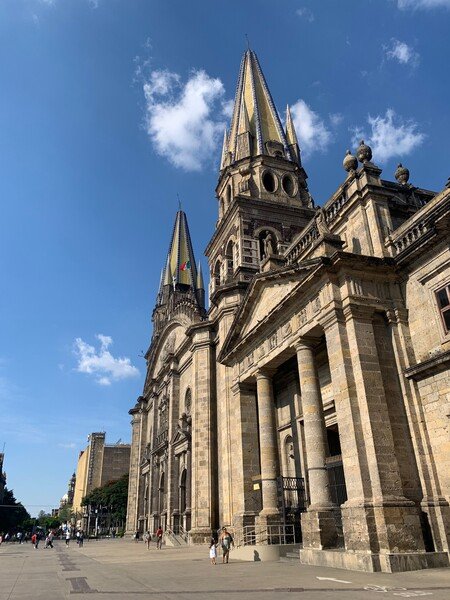 A picture of Guadalajara, Mexico's Cathedral with a bright blue sky and some people walking by.