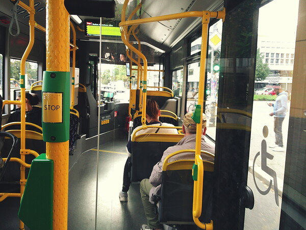 Public bus interior with passengers, yellow pole, and wheelchair sign.