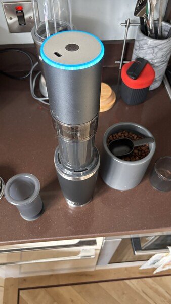 Step two. Grinding. The burr grinder has an active blue light ring. A different angle than step one. More from the side showing the tower of cup, AeroPress, and grinder. 