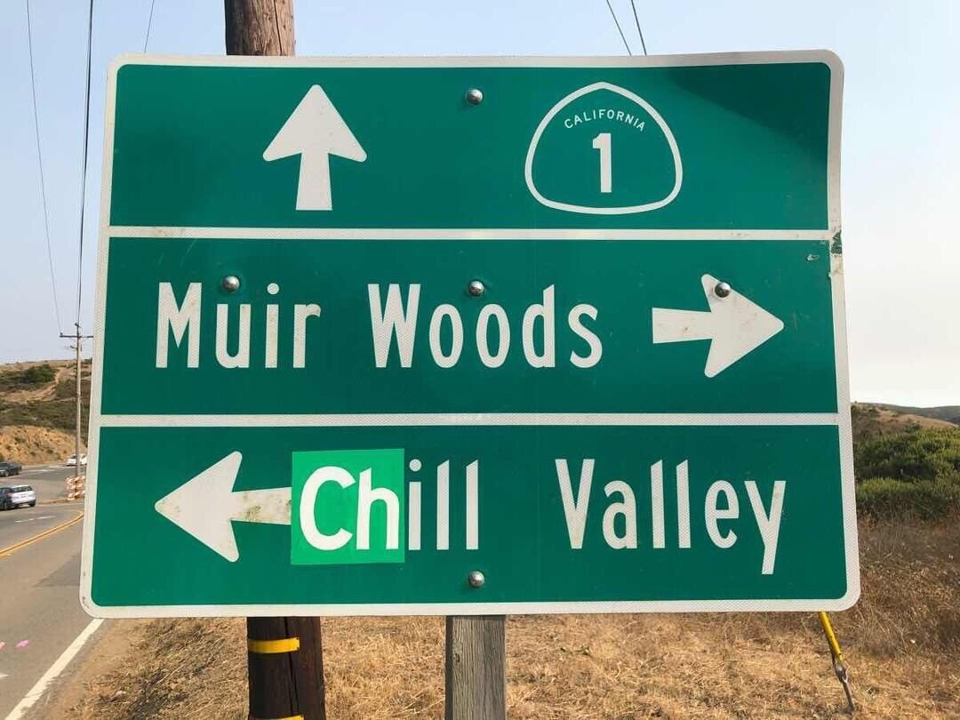 A picture of a road sign in at the 'Four Corners' intersection in  Marin where the legend 'Mill Valley' has been altered to read 'Chill Valley'