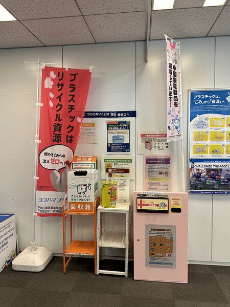 A white hall at a Japanese ward office, with recycling signs, posters, and collection boxes.