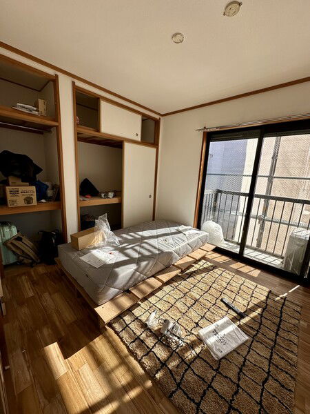 Japan apartment bedroom with partially constructed bed, balcony, and wooden floor.