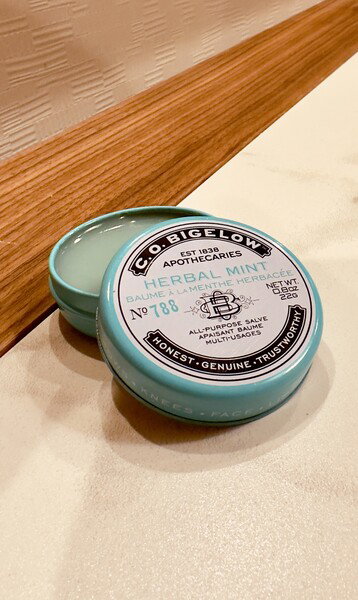 A blue tin of mint herbal balm is on a table.