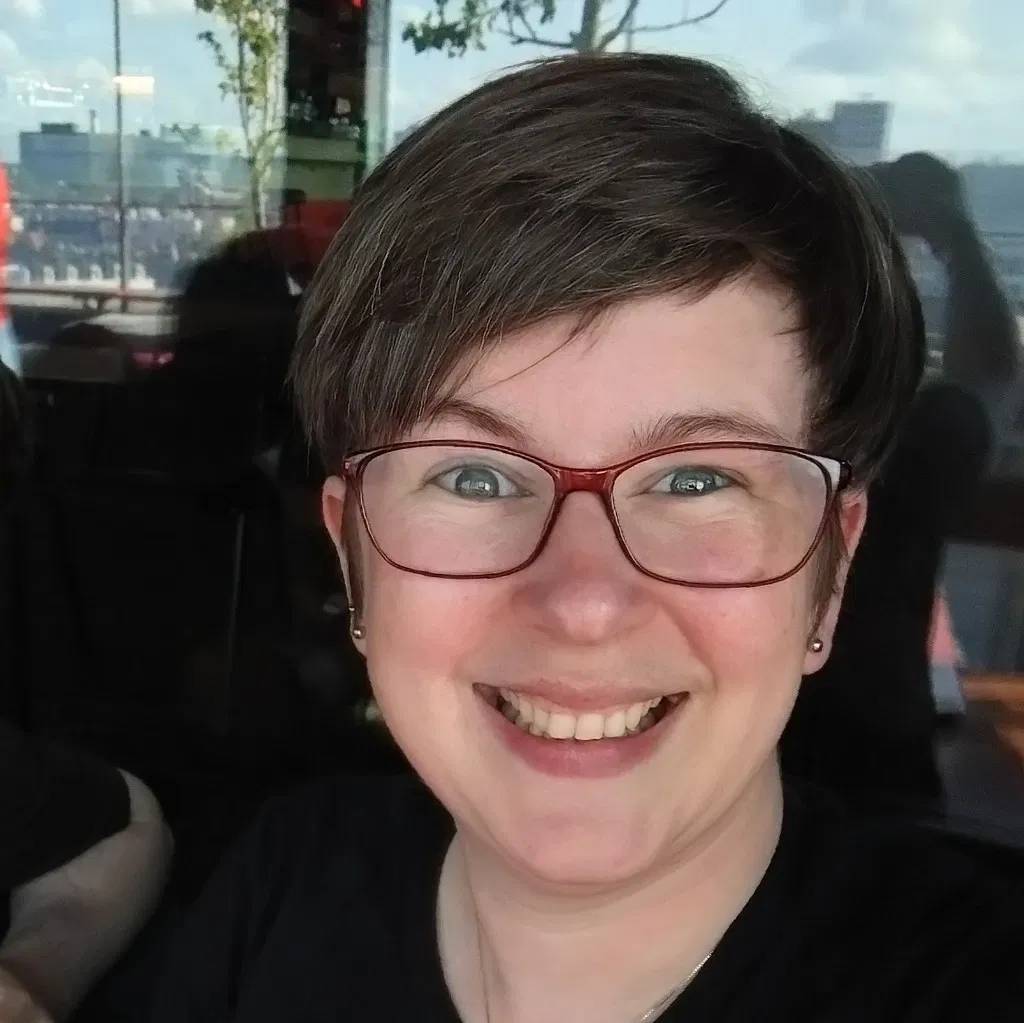 A smiling picture of me with my standard sideswept short hair and red framed glasses.
