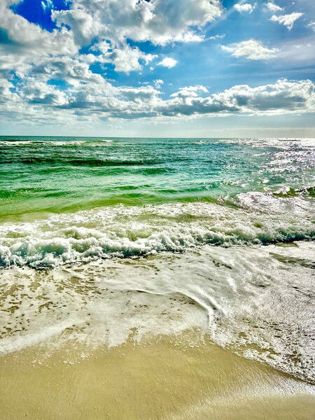 Waves lapping the beach on a sunny day, blue sky, white clouds, turquoise water. Gulf Shores, AL