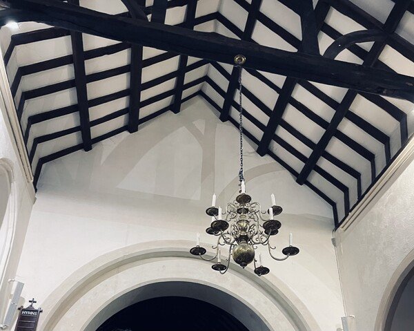 photo of the ceiling of a church, with black beams and white plaster, and a chandelier with candles
